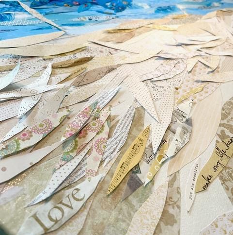 Detail of the collage's sandy beach — layered cream and gold paper strips of lace, sheet music, florals, and the word 'Love'.