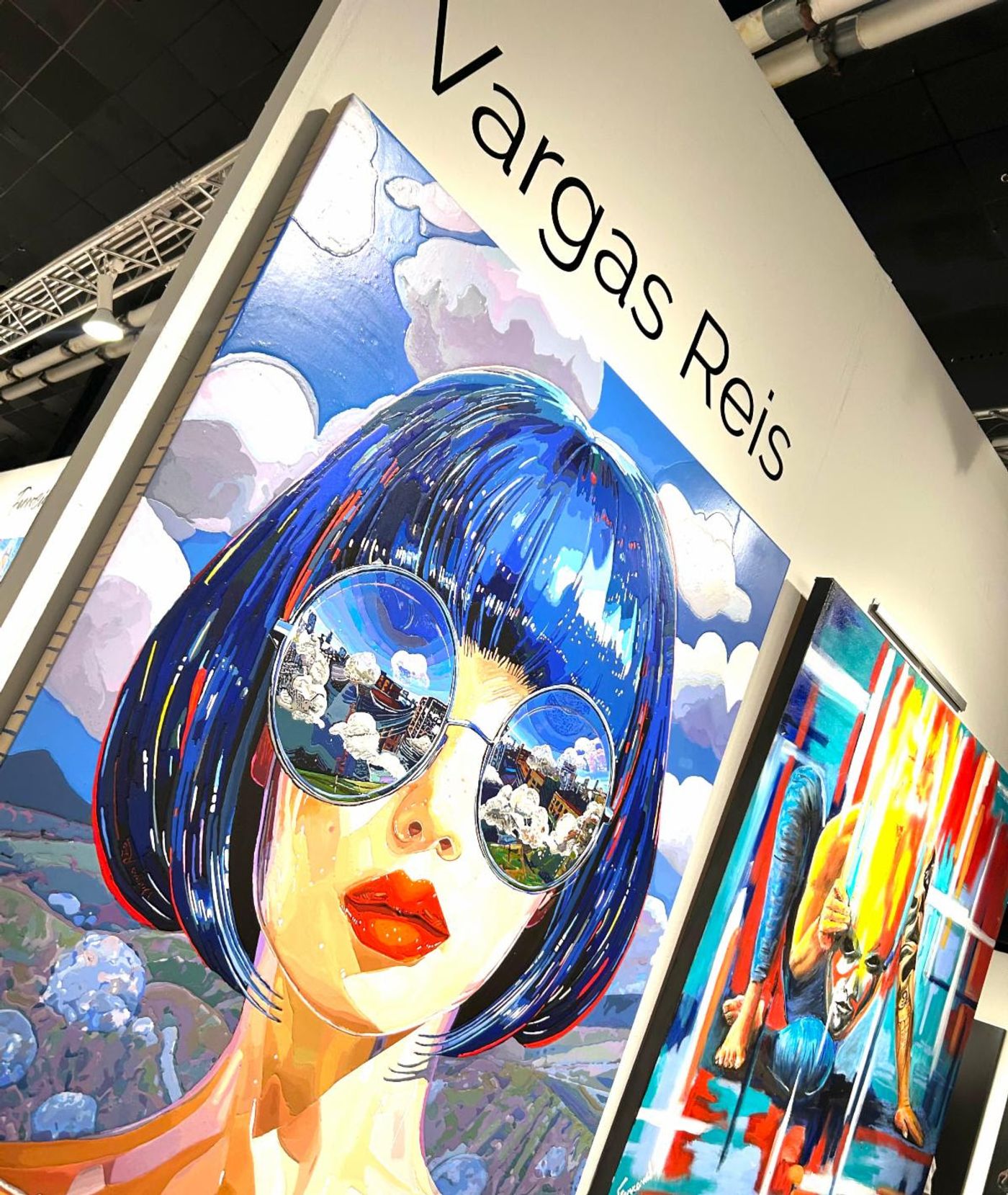 Vargas Reis booth — a huge portrait of a blue-bobbed woman, her round mirrored sunglasses reflecting clouds and a city.