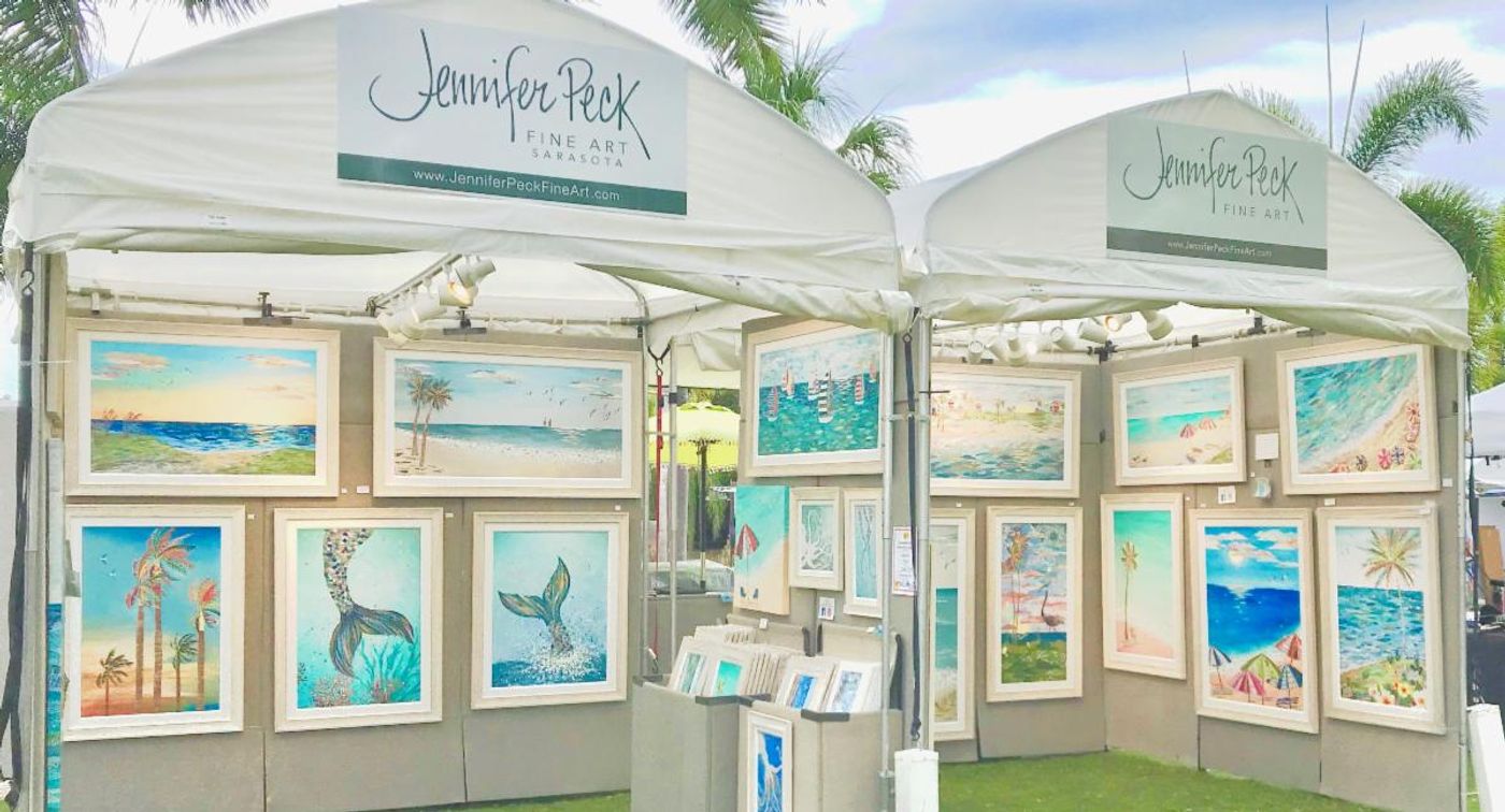 Jennifer Peck Fine Art booth — two white festival tents hung with framed coastal collages on gray walls, palms overhead