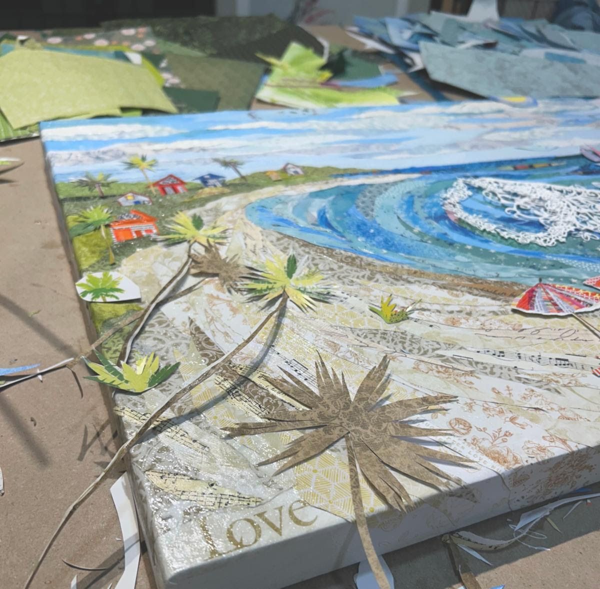 Close view of Sunny Days in progress — palm trees hand-cut from sheet music and toile papers leaning over the sand