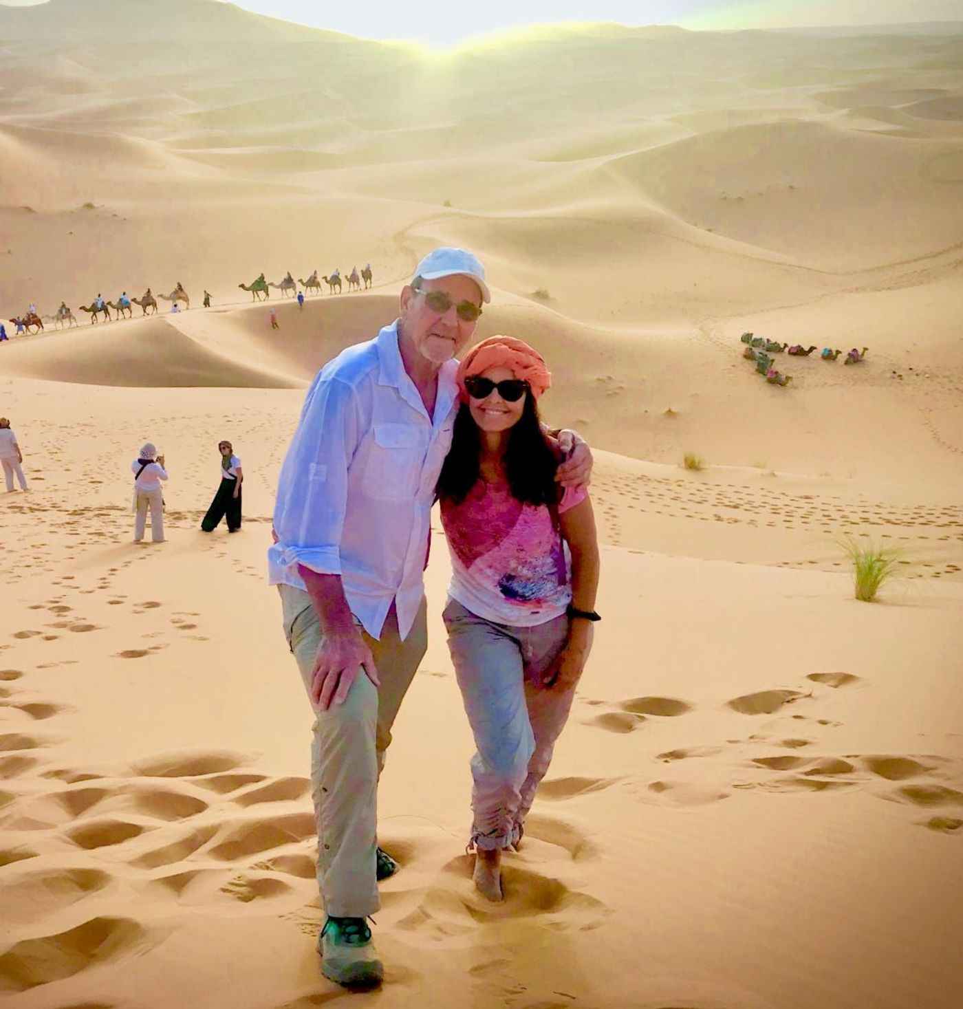 Jennifer and Steve on the dunes of the Sahara during their summer trip to Morocco, a camel caravan behind
