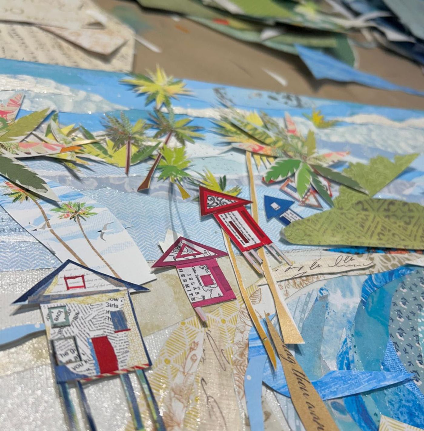 Beach cottages snipped from newsprint and patterned papers under paper palms — a corner of "Sunny Days" mid-build