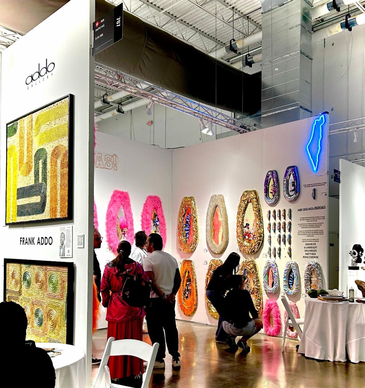 Addo Gallery booth in Miami — Frank Addo's textured canvases beside a wall of gilded, feather-trimmed papaya reliefs.