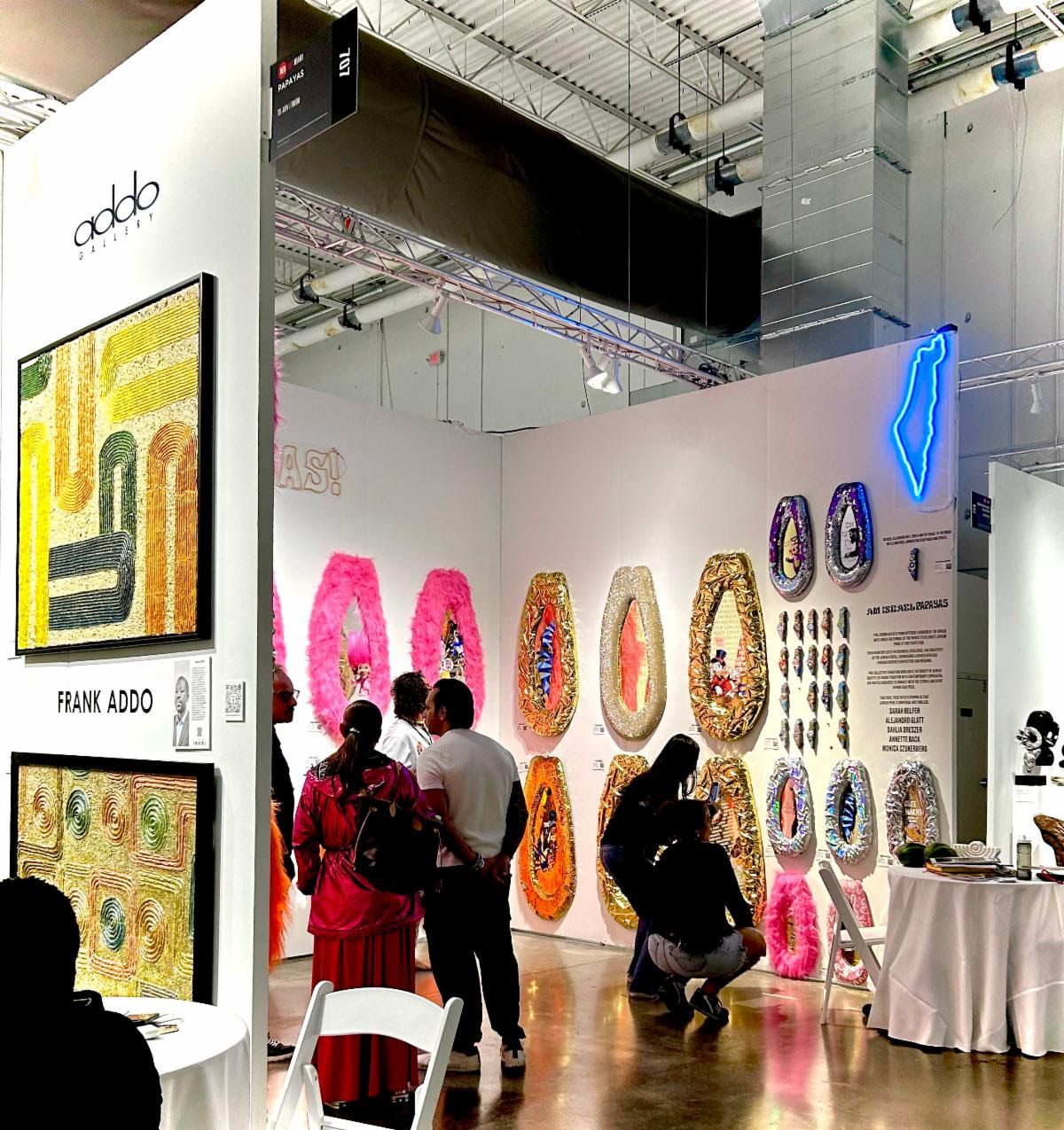 Addo Gallery booth in Miami — Frank Addo's textured canvases beside a wall of gilded, feather-trimmed papaya reliefs.