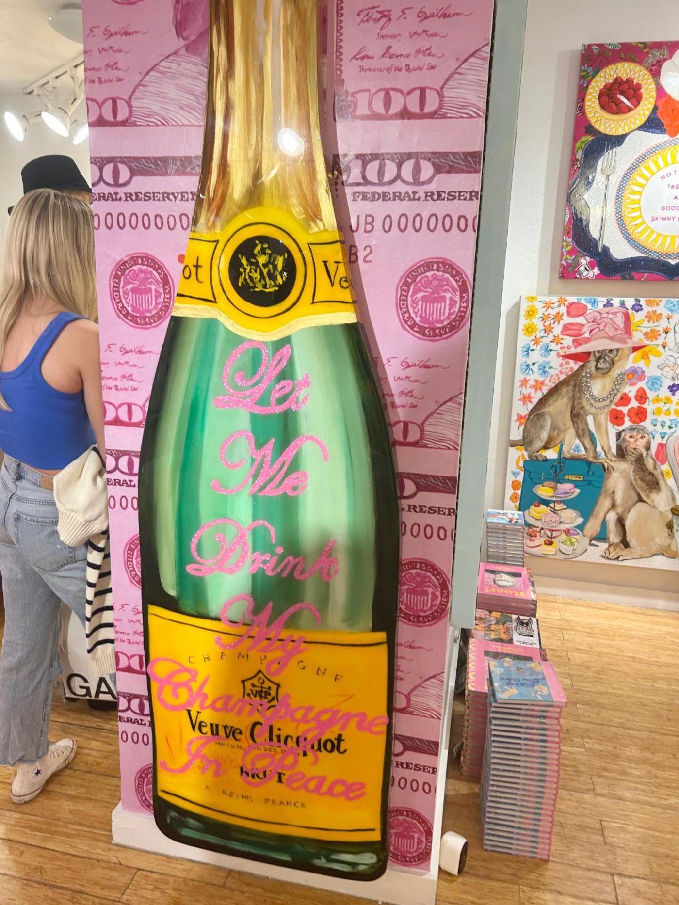 A towering Veuve Clicquot bottle cutout reading 'Let Me Drink My Champagne In Peace' on pink hundred-dollar-bill wallpaper.