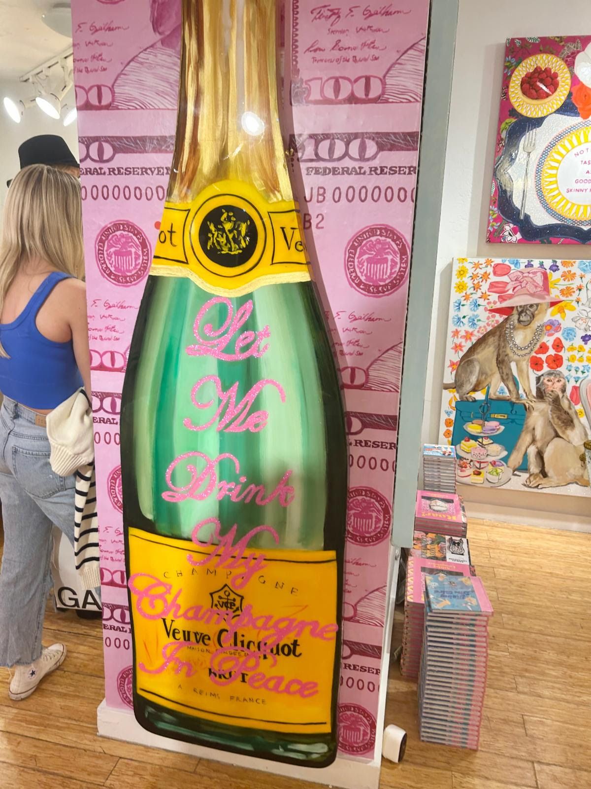 A towering Veuve Clicquot bottle cutout reading 'Let Me Drink My Champagne In Peace' on pink hundred-dollar-bill wallpaper.