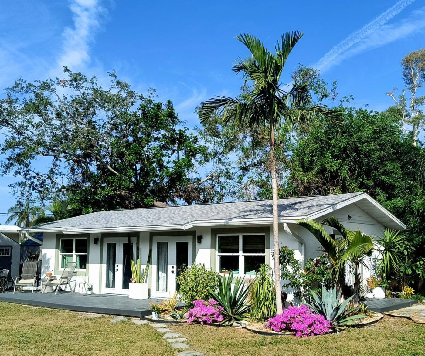 Jennifer's white home studio behind its garden — palm tree, agaves, magenta bougainvillea, and a gray deck under a blue sky.