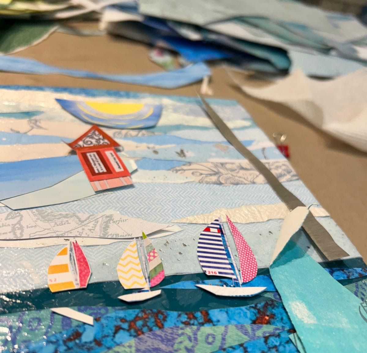 Detail of tiny paper sailboats with striped and patterned sails crossing layered blue water, a sun rising behind