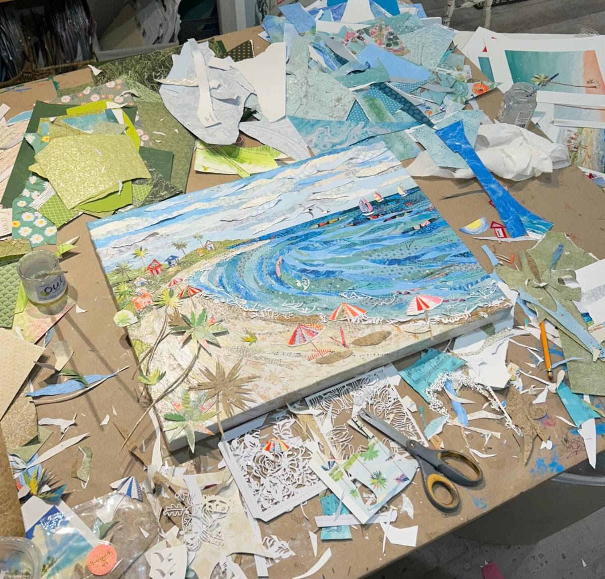 The Sunny Days canvas on Jennifer's worktable, surrounded by paper scraps, scissors and a jar of glue