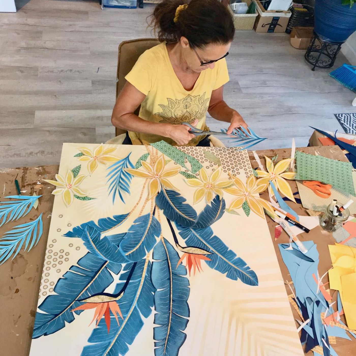 Jennifer cuts a blue paper palm frond by hand while assembling a botanical collage in the studio