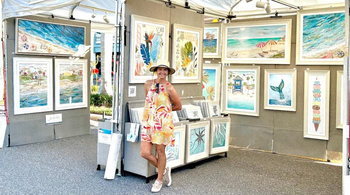 Jennifer in a sun hat at her festival booth, walls hung with framed coastal collages — beach scenes, a mermaid tail, an ice cream stack