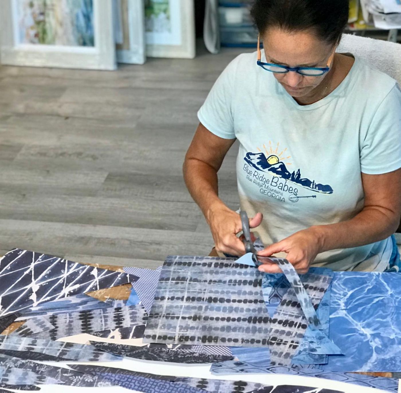 Jennifer cutting strips of blue patterned paper with scissors at a table layered in indigo and watery-blue prints