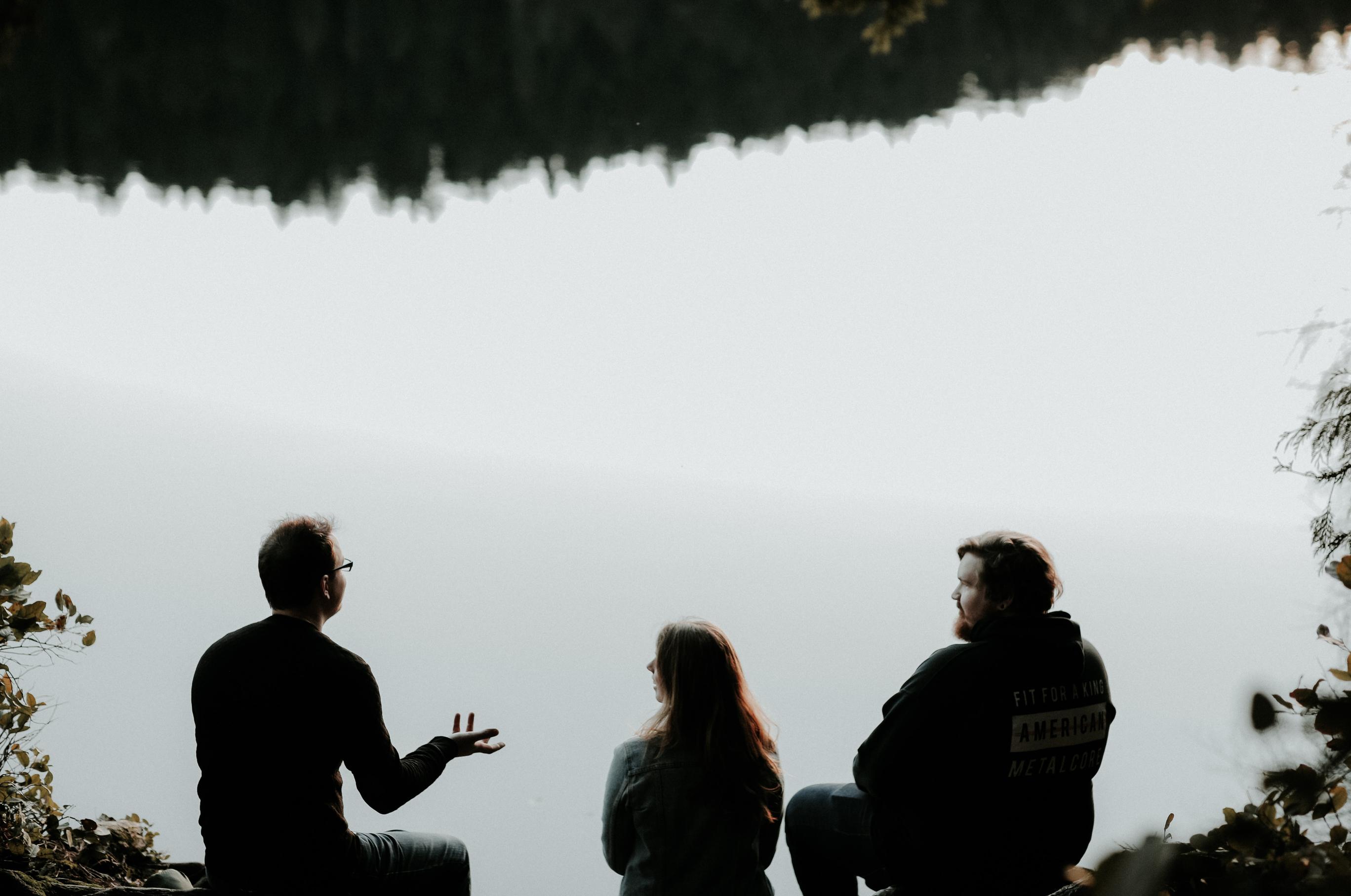 Tre mennesker snakker sammen. Vi ser dem bakfra og i bakgrunnen er en stor innsjø.