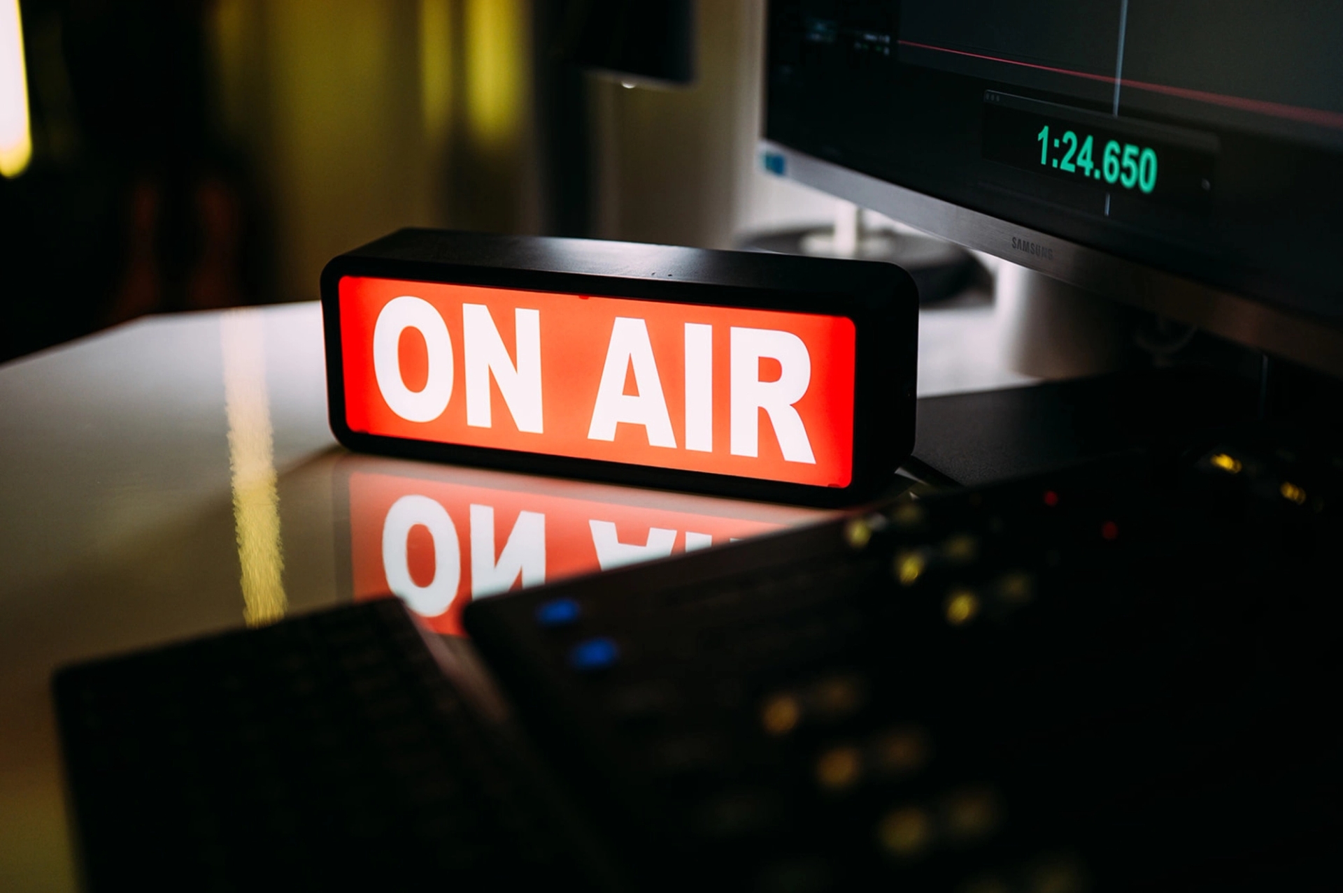 An illuminated ON AIR sign on a studio desk beside a monitor