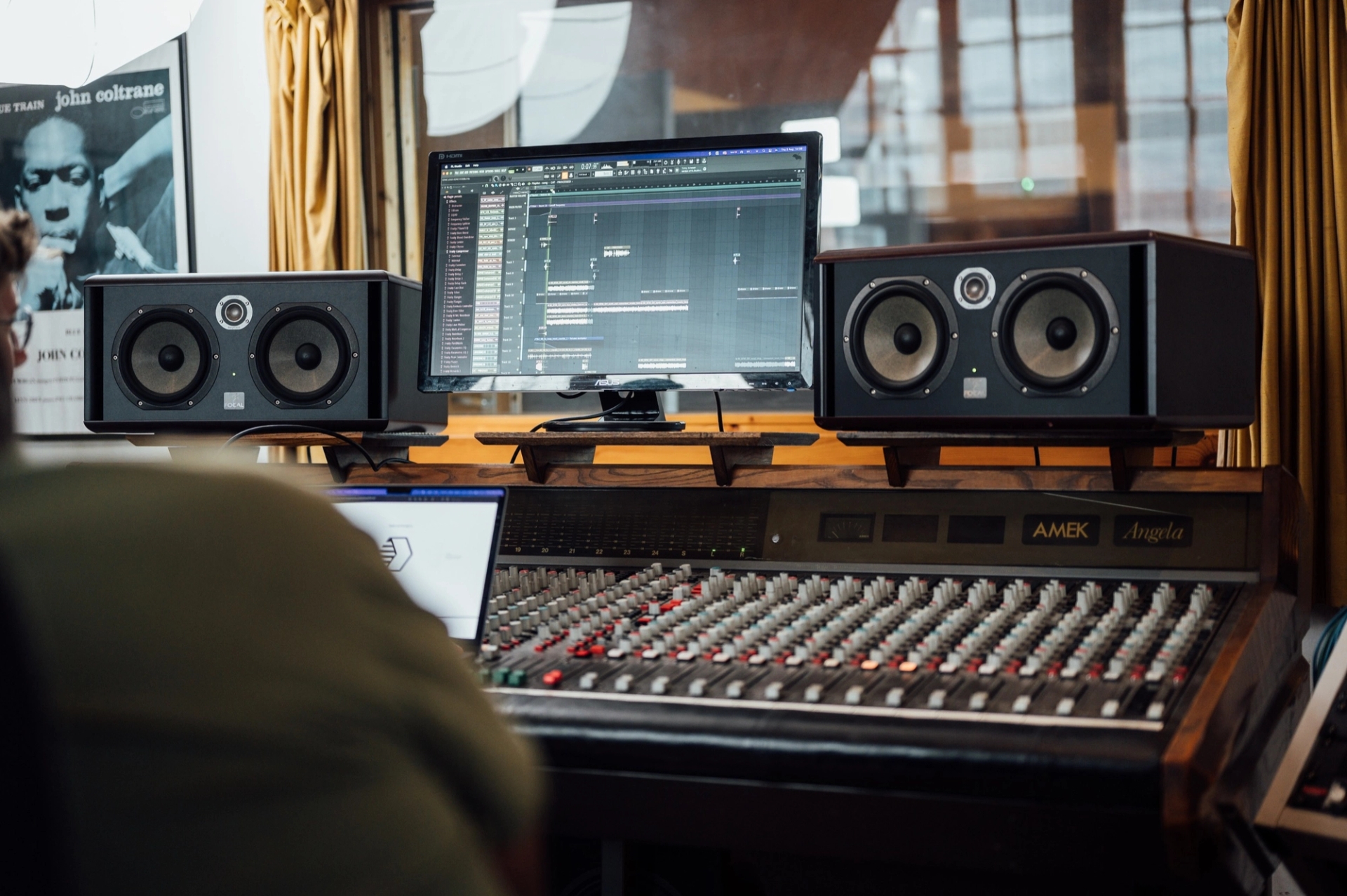 A studio desk with monitor speakers, a mixing console and a screen showing a music session