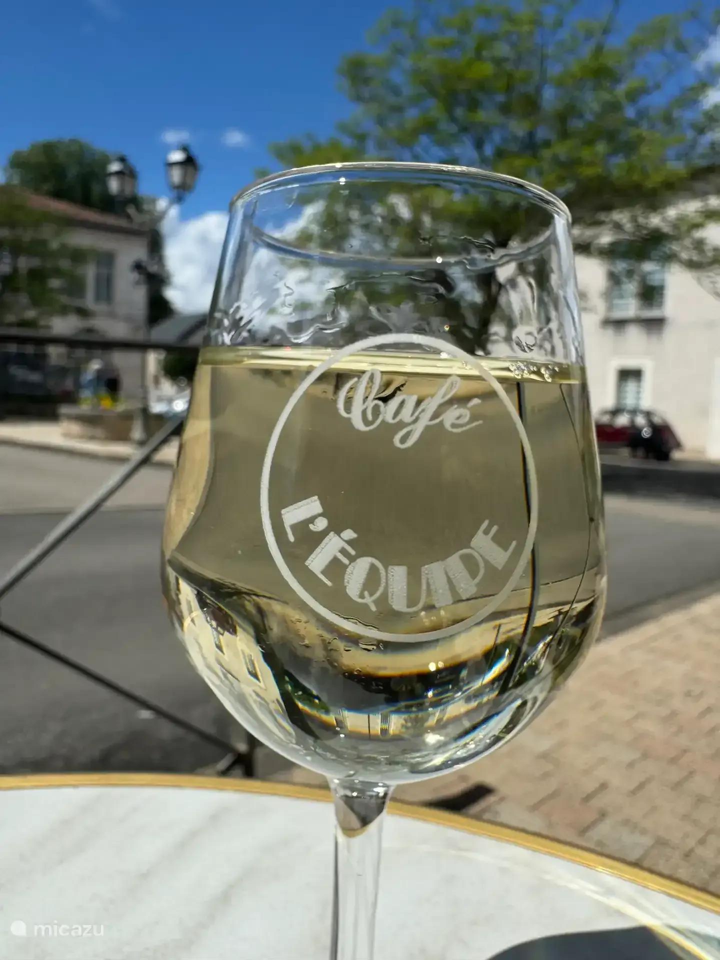 Een glas witte wijn op een cafétafel aan een dorpsplein