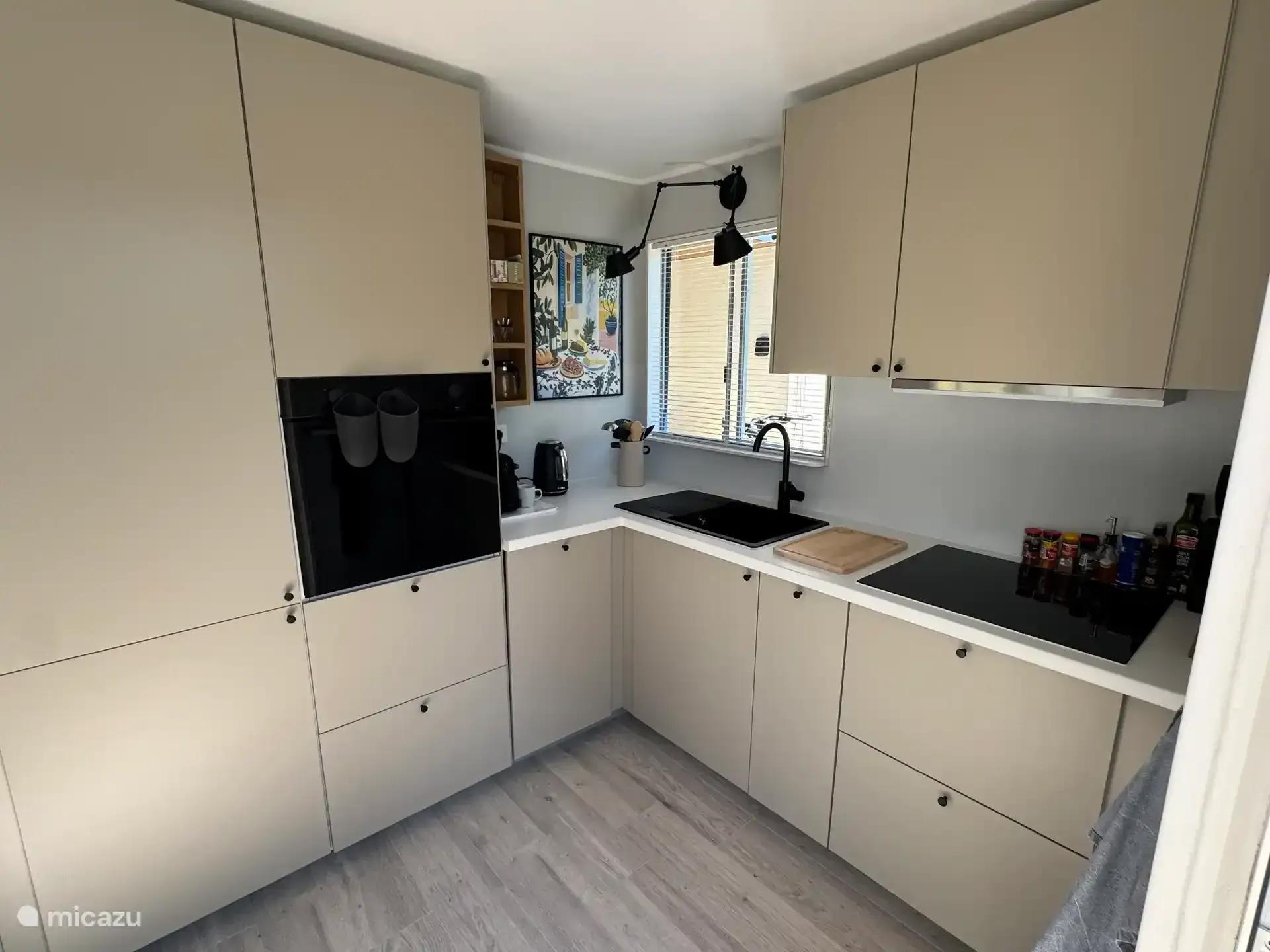 De open keuken met inductiekookplaat, oven en lichte kastenwand