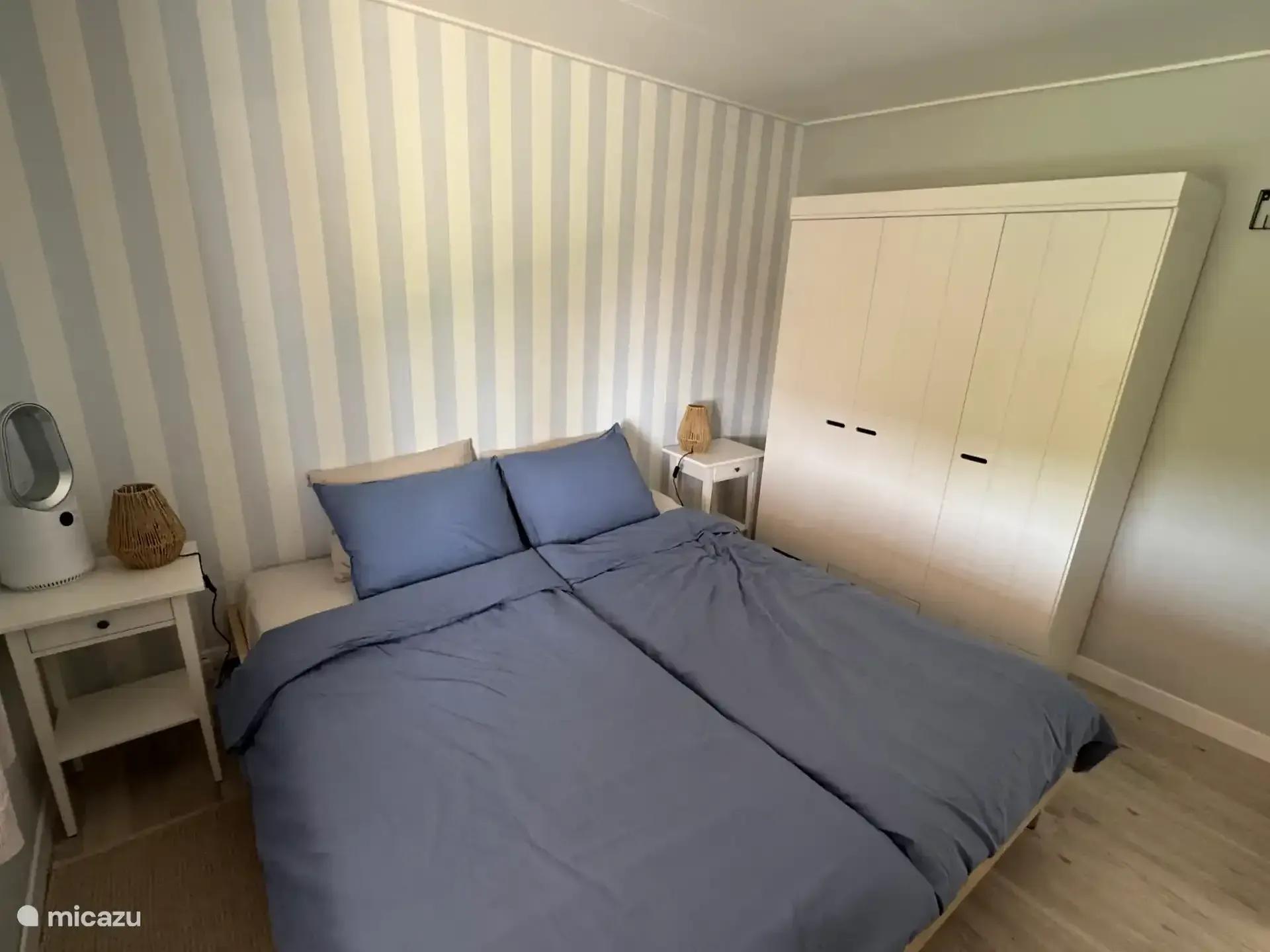 Slaapkamer met bed, inbouwkast en gestreept behang