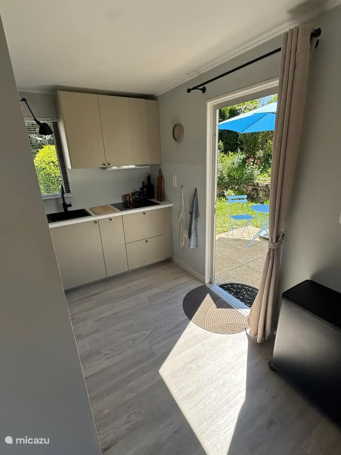 Doorkijk vanuit de hal langs de keuken naar de open deur en het zonnige terras