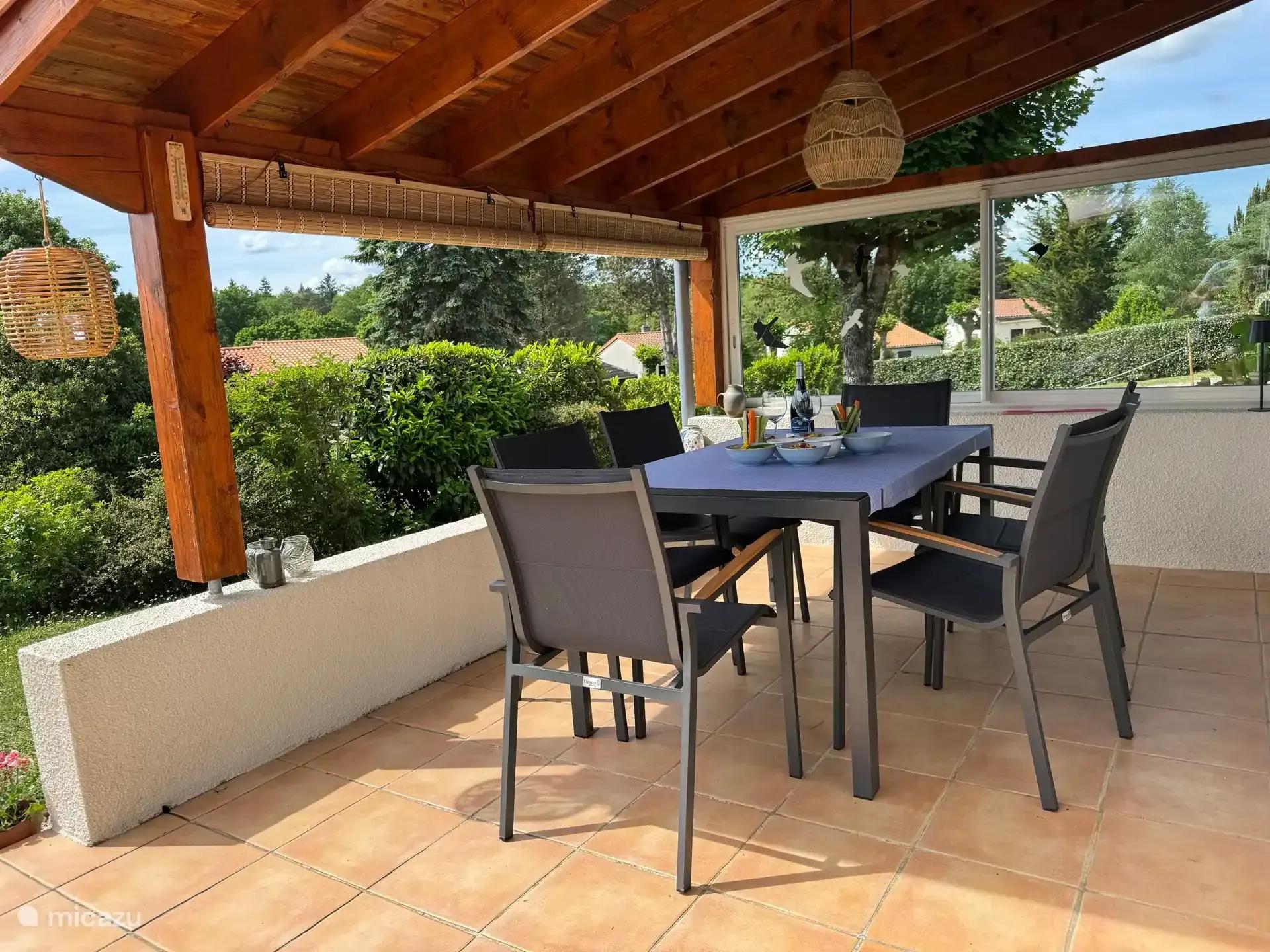 Het overdekte terras met houten balken, een eettafel en zes stoelen