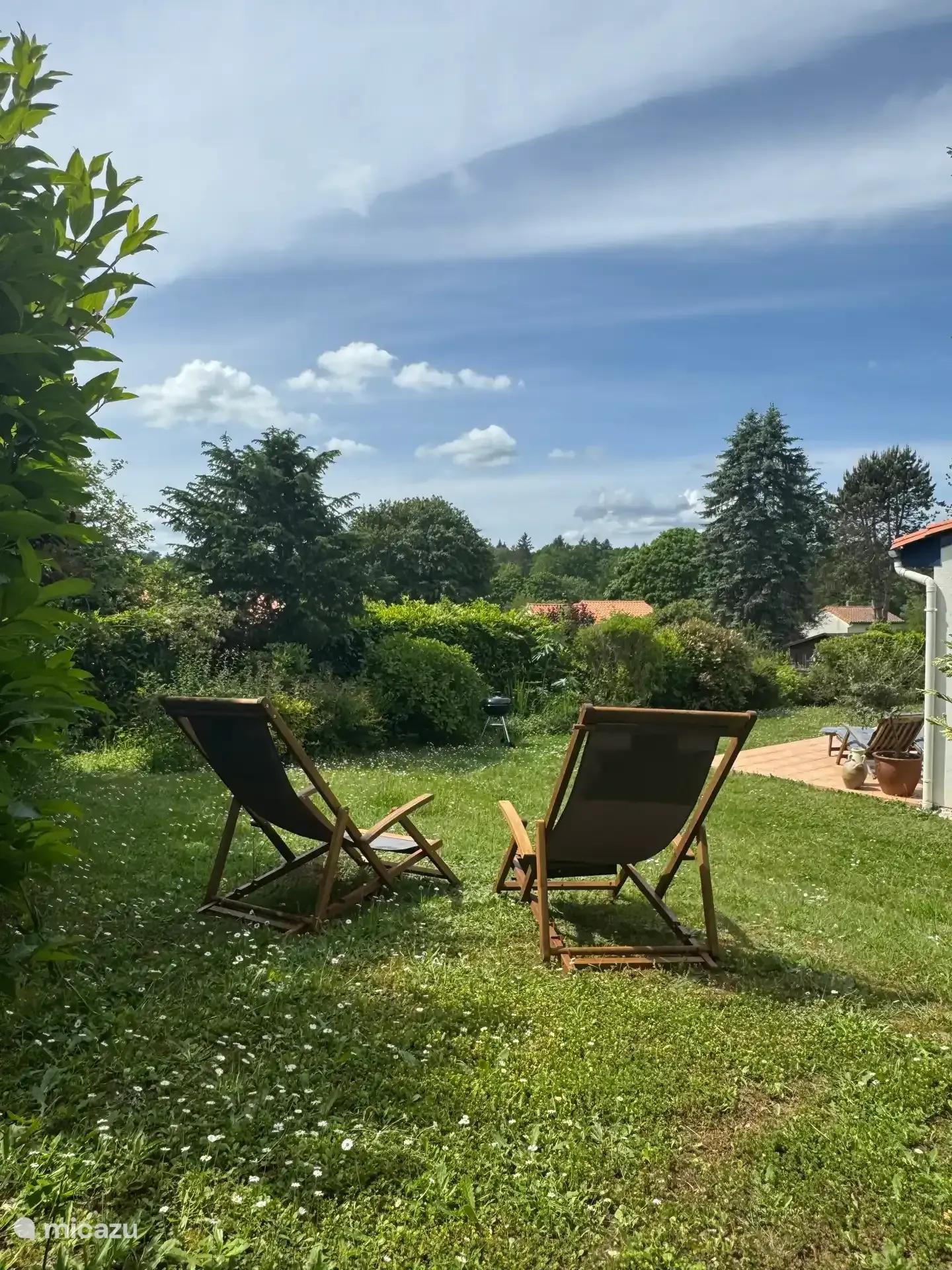 Twee houten ligstoelen in het gras achter het huis, met bos op de achtergrond