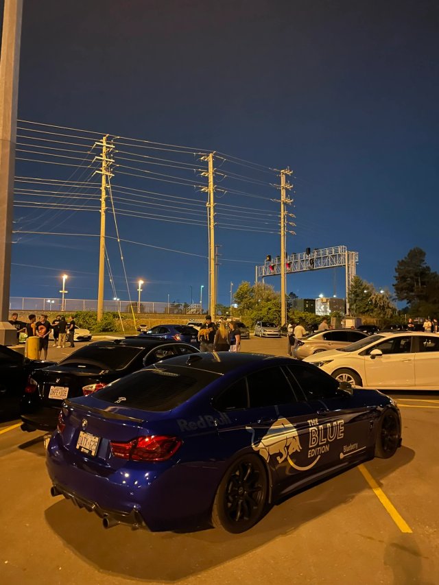 A blue sedan with Red Bull graphics parked among cars at dusk