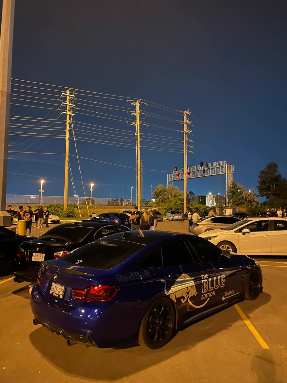 A blue sedan with Red Bull graphics parked among cars at dusk