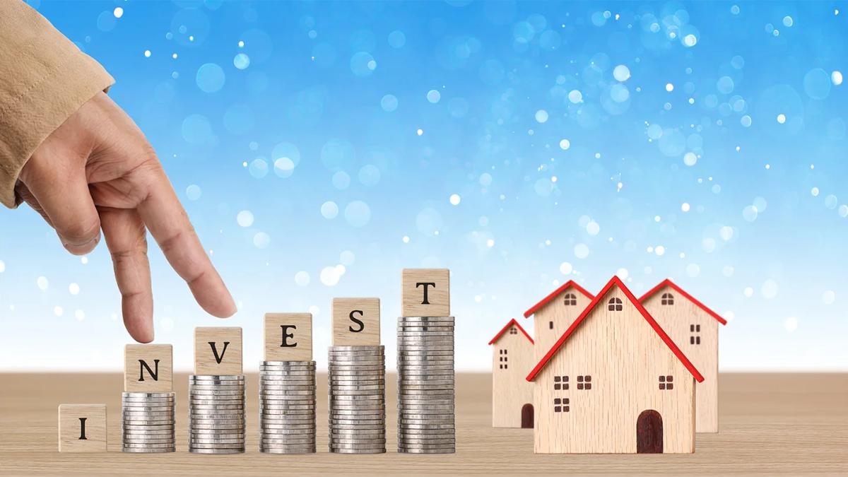 Stacked coins labelled investment beside model houses, symbolising strategic real estate investment growth.