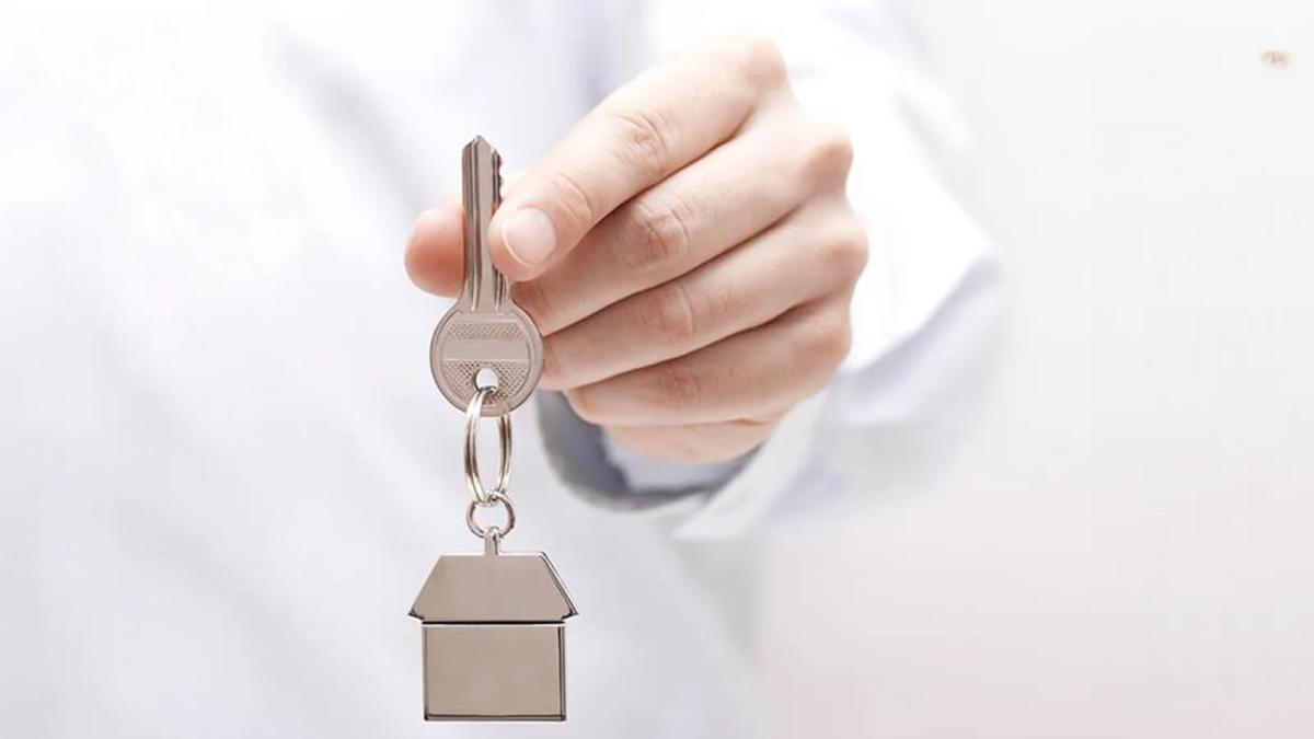 Hand holding a house key with a home-shaped keychain, symbolising home ownership.