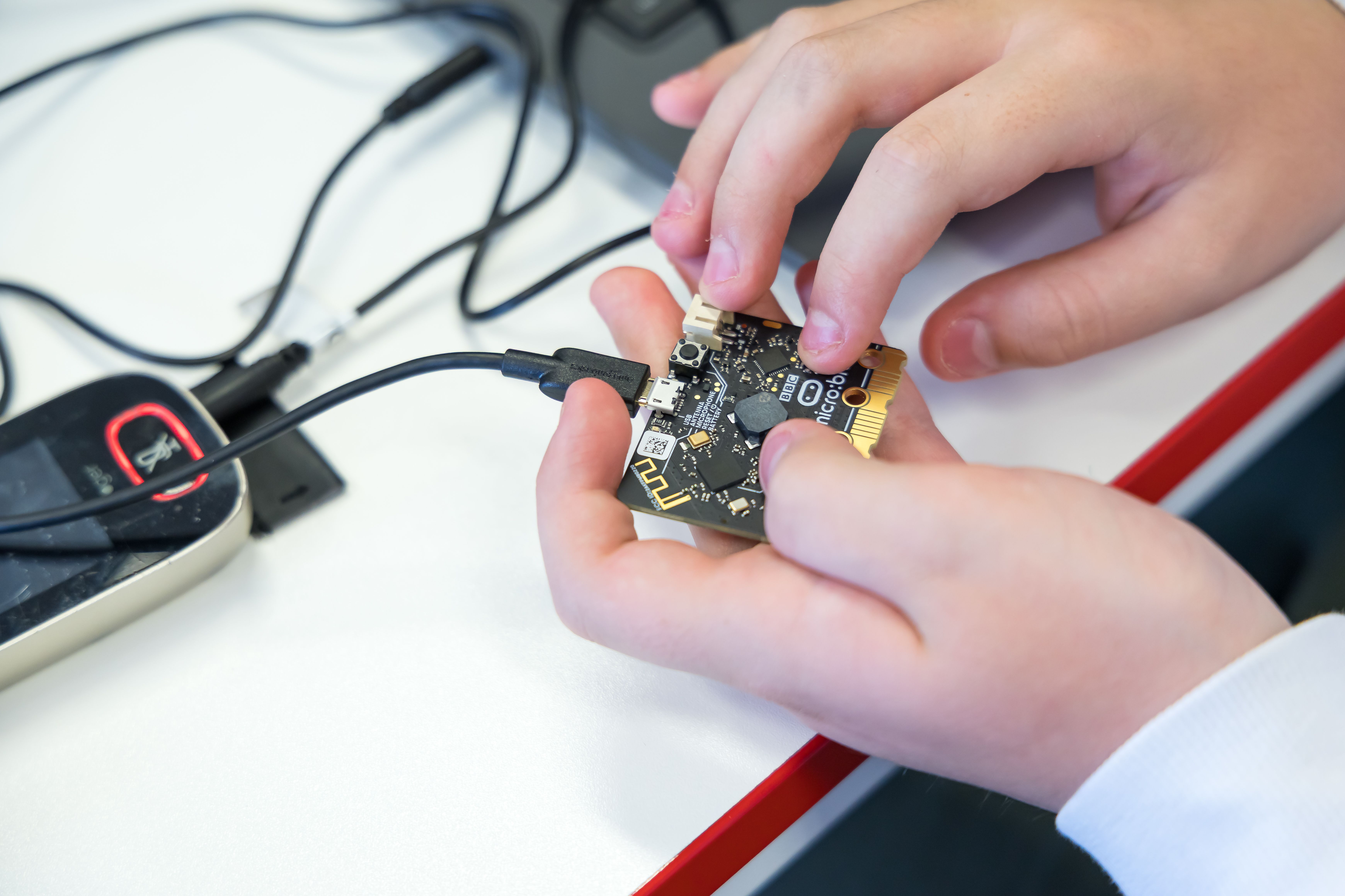 A pair of hands holding a micro:bit with back facing upwards and a USB cable attached