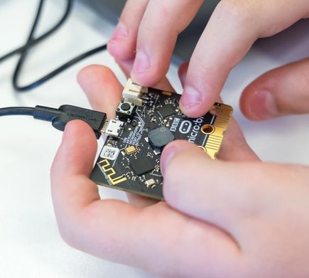 A pair of hands holding a micro:bit with back facing upwards and a USB cable attached