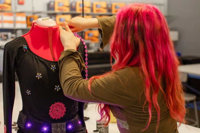 A female student attaches the final touches to the clothing on a mannequin. The belt, connected to a micro:bit, is lit up