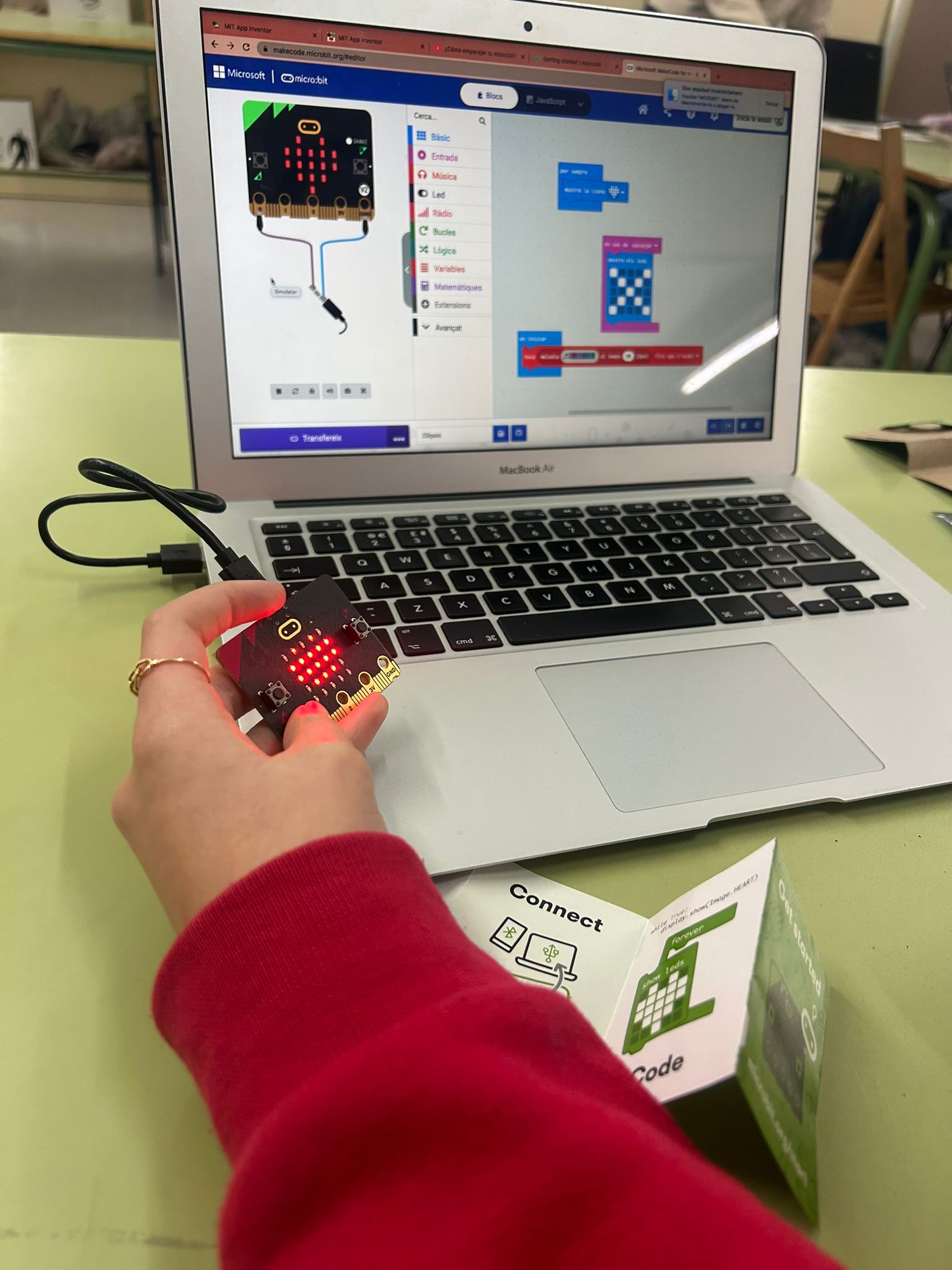 Student demonstrates the Butterfly project holding a micro:bit in one hand and showing the code on their computer screen. 