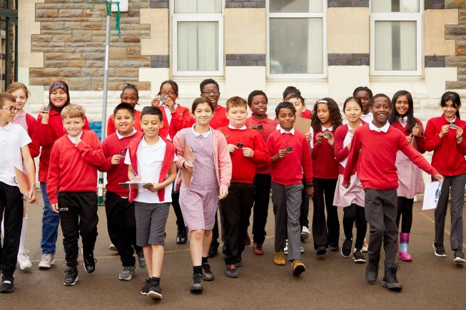A group of primary school aged children walking across a playground, micro:bits in hand, ready to participate in the playground survey