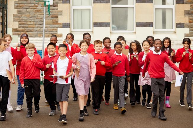 A group of primary school aged children walking across a playground, micro:bits in hand, ready to participate in the playground survey