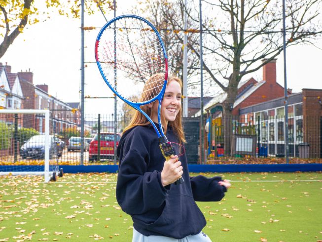 Student holds a tennis racket fitted with a micro:bit, using it to measure movement and explore performance during play.