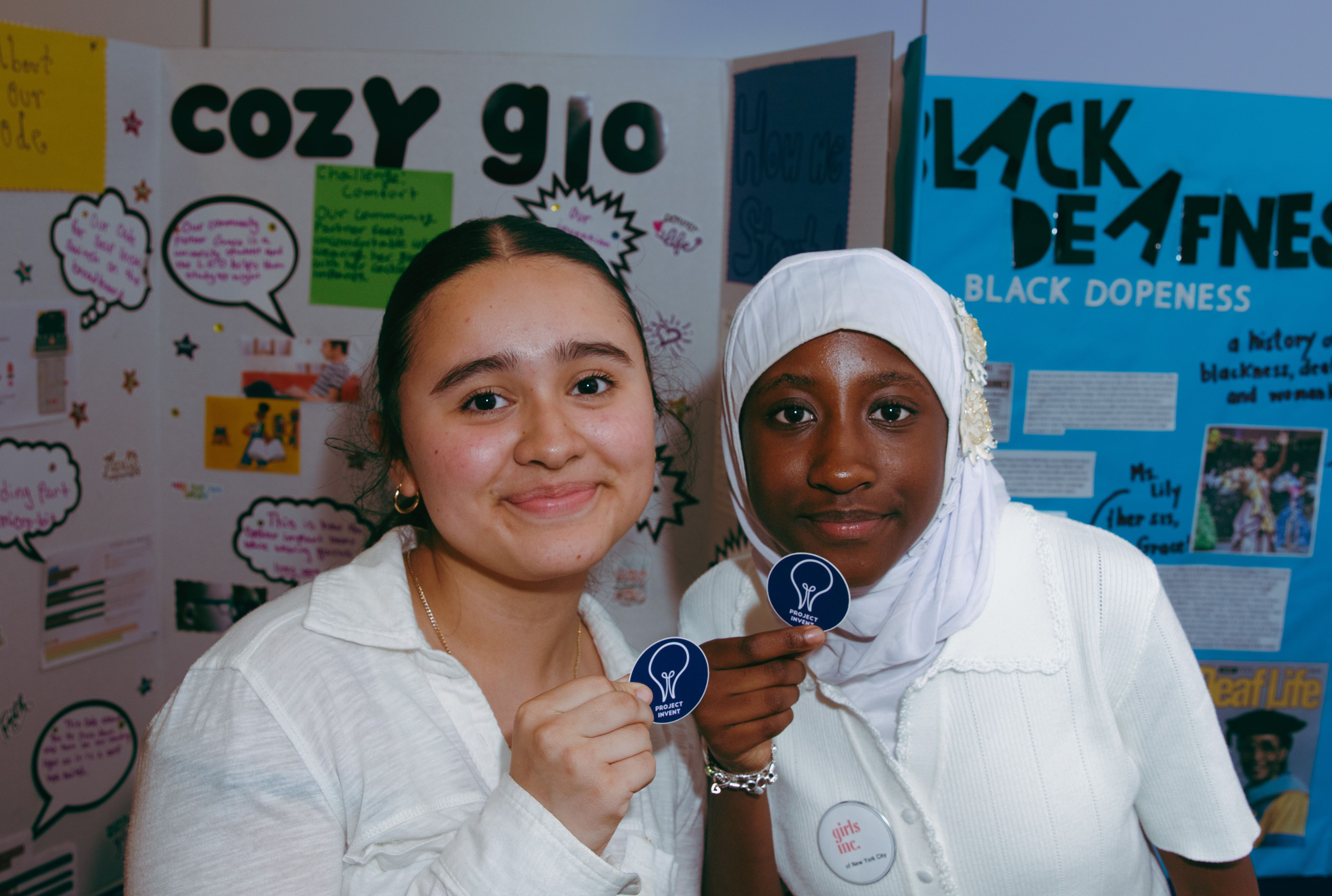 Two students posing in front of the cozy glo project board. 