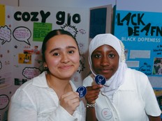 Two students posing in front of the cozy glo project board.