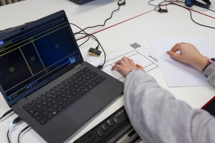 A student feeling a tactile diagram of the MakeCode editor with one hand and a tactile key for the editor with the other, both embossed using a braille embosser.