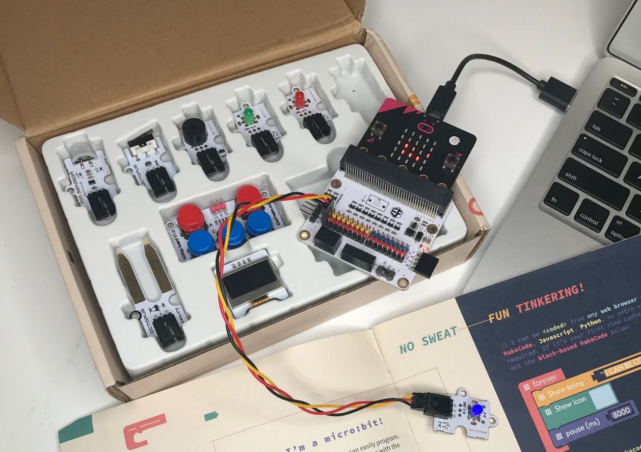 A Tinker Kit in a box, showing a micro:bit attached to the edge connector and to a computer via USB cable. There are various buttons, LEDs and other components in the box. 
