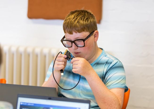A student exploring a micro:bit with braille capital A and B labels above the buttons.