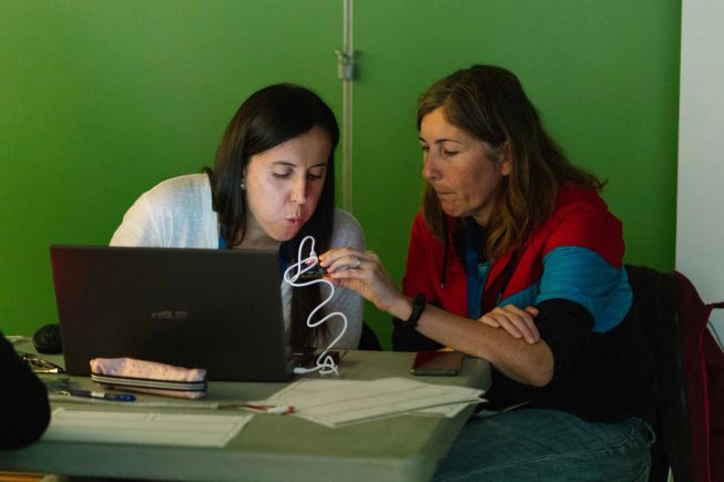 Two female teachers are coding a micro:bit, one is blowing into it to try the candle project.