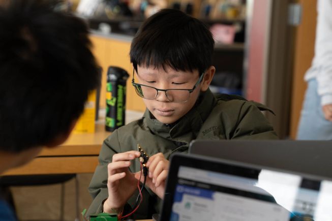 A student holds his micro:bit thoughtfully as he is coding it