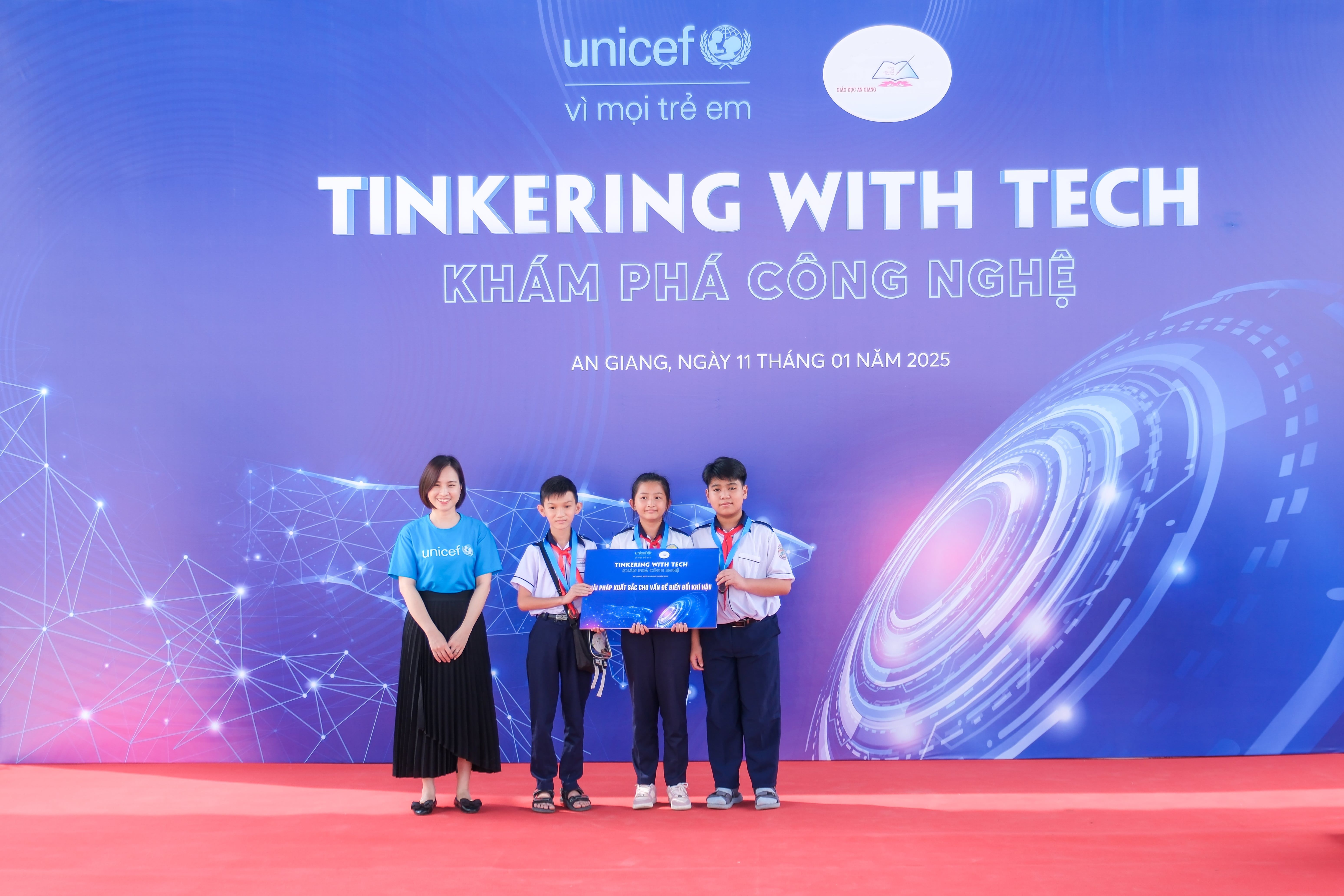 Students and their teacher pose in from of a "Tinkering with Tech" sign.