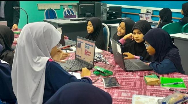 A group of girls are sat round some laptops connected to their micro:bits, they are coding with deep concentration