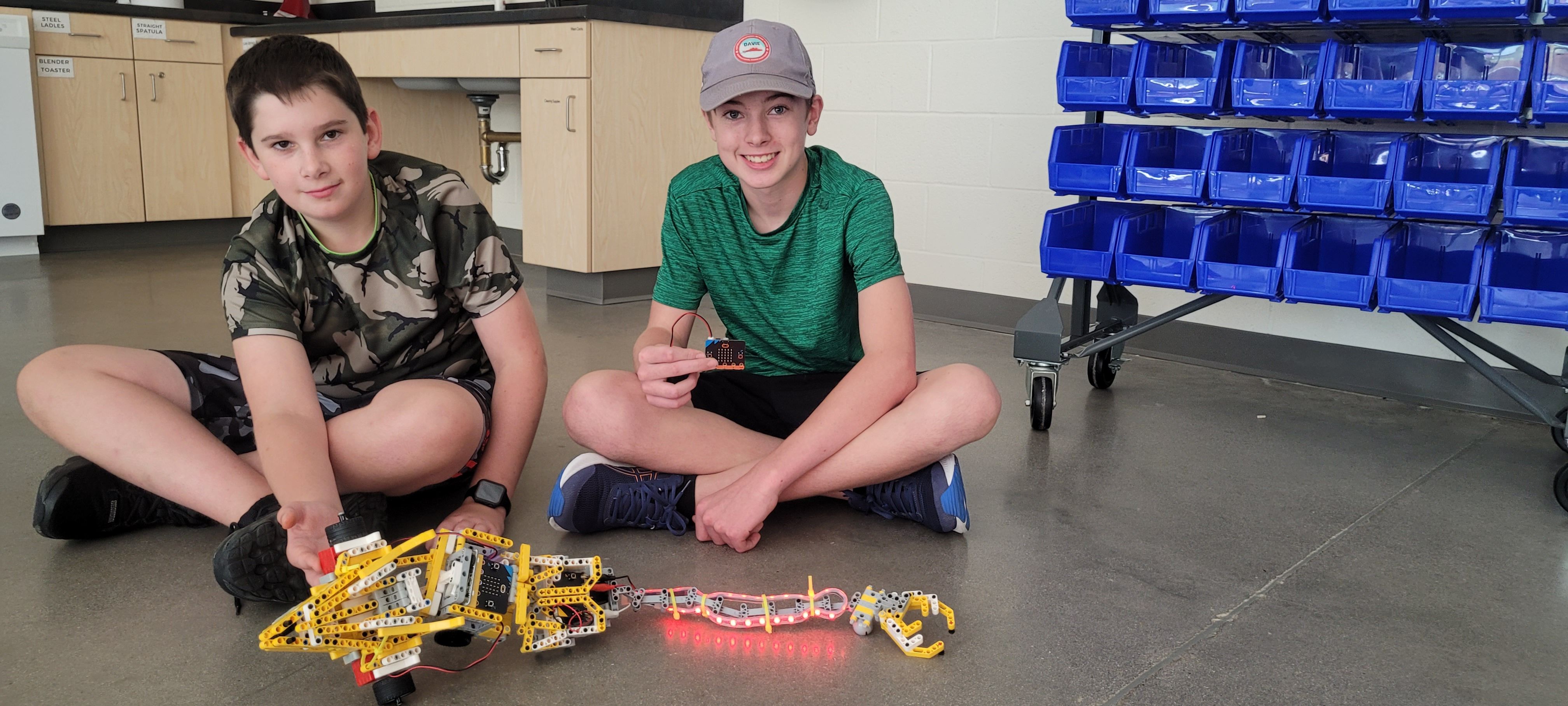 Students sit on the floor showing the car they built.