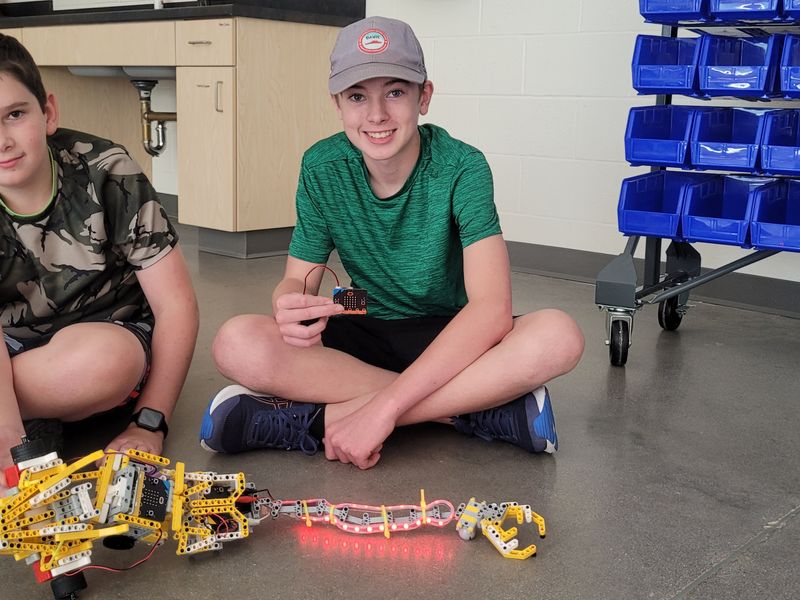 Students sit on the floor showing the car they built.