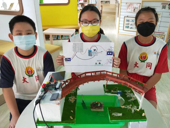 Three children from Taiwan sit around their micro:bit creation
