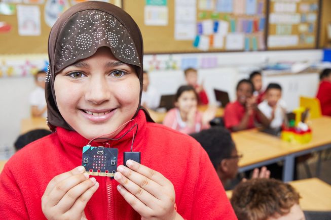A girl holds her micro:bit excitedly in the classroom