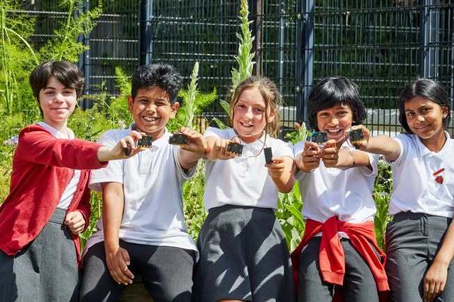 5 children holding up micro:bits and battery packs outdoors